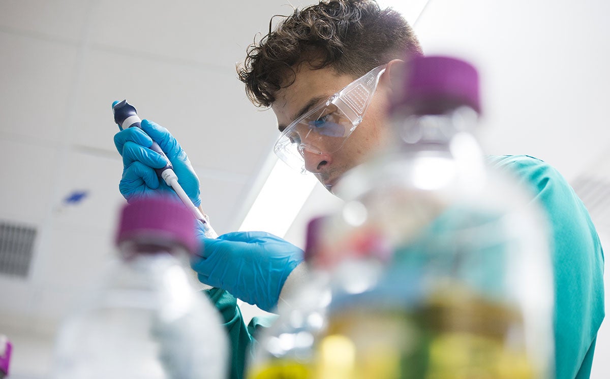 Student in a lab using a pipette to add liquid to a container